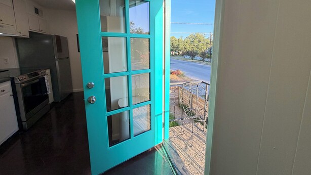 A kitchen with a teal door, stainless steel appliances, and a view of a street and greenery outside. - Peaceful Hyde Park Condo Near UT/Moody with Free Parking, Fast WiFi, King Bed (Austin)