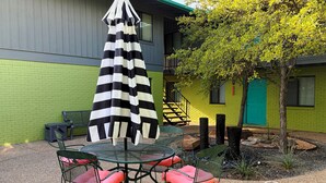 A patio with a table and chairs, a striped umbrella, and a green brick wall. - Peaceful Hyde Park Condo Near UT/Moody with Free Parking, Fast WiFi, King Bed (Austin)