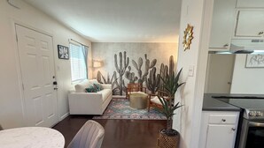 A living room with a white sofa, a round dining table, and a kitchen area with a stove. - Peaceful Hyde Park Condo Near UT/Moody with Free Parking, Fast WiFi, King Bed (Austin)