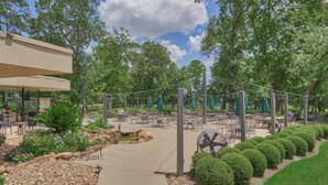 Un espace extérieur abrité, aménagé avec des tables et des chaises, entouré d’arbres et bordé d’un sentier.