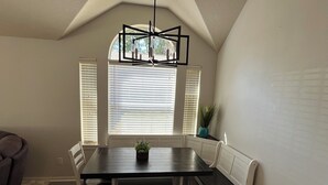 Un coin repas avec une table en bois foncé, des bancs blancs et une plante en pot.