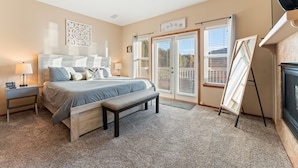 A bedroom with a bed, bench, bedside tables, and a large window with blinds.