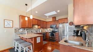 A modern kitchen with wooden cabinets, a central island with bar stools, stainless steel appliances, and a skylight.