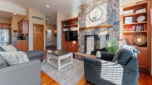 A modern living room with a stone fireplace, grey sofas, a coffee table, and a bookshelf.
