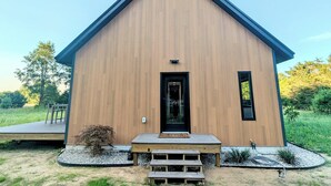 Une cabane moderne en bois, dotée d’un toit en pente, d’une porte d’entrée et d’une petite terrasse avec des bancs.