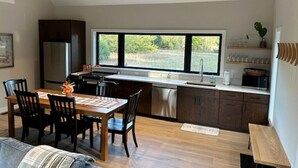 Une cuisine moderne avec des poutres en bois, un coin repas avec une table et des chaises, et une grande fenêtre donnant sur un paysage verdoyant.