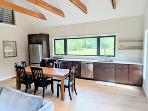 A modern kitchen with a dining area, wooden beams, a large window, and a map on the wall.