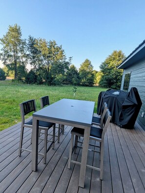 A deck with a table and chairs, a barbecue grill, and a grassy yard with trees.