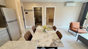Une cuisine moderne dotée d’un réfrigérateur encastré, un coin repas avec une table en marbre et des chaises marron, et un espace détente avec un fauteuil en cuir.