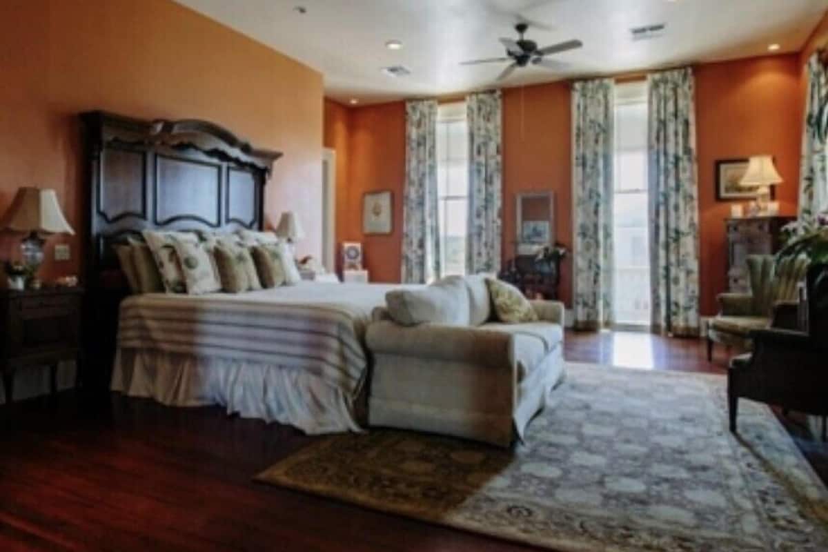 A bedroom with a large bed, a chair, a ceiling fan, and a window with curtains.