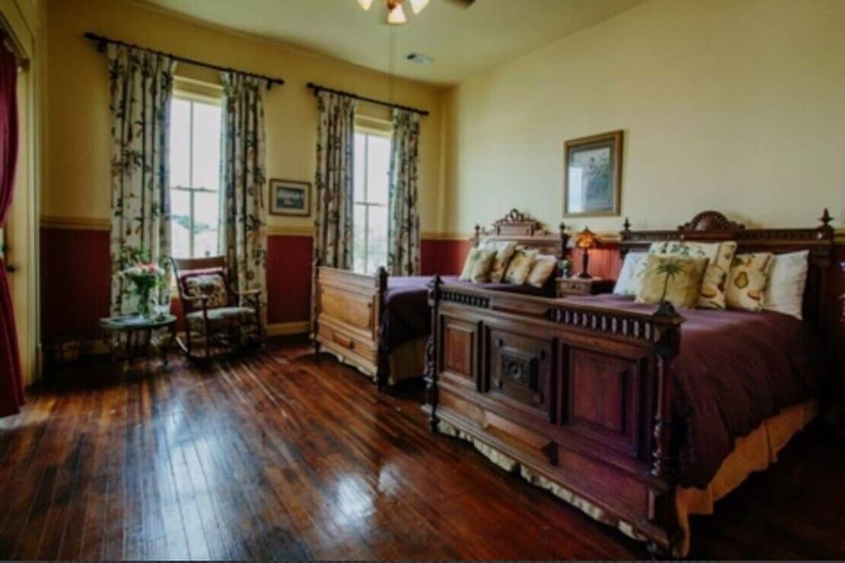 A traditional bedroom with a wooden bed, a nightstand, a chair, and a window with curtains.