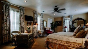 A bedroom with a bed, a desk, a chair, a television, and a ceiling fan. - The Lasker Inn - B&B (Galveston)