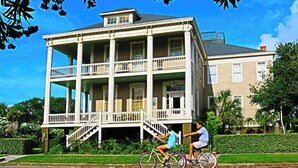 A two-story building with a balcony on the second floor, a staircase leading to the entrance, and a well-maintained lawn. - The Lasker Inn - B&B (Galveston)