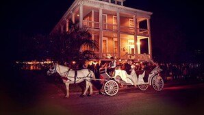 A white carriage pulled by two horses, parked in front of a large, illuminated building with multiple balconies and a grand entrance. - The Lasker Inn - B&B (Galveston)