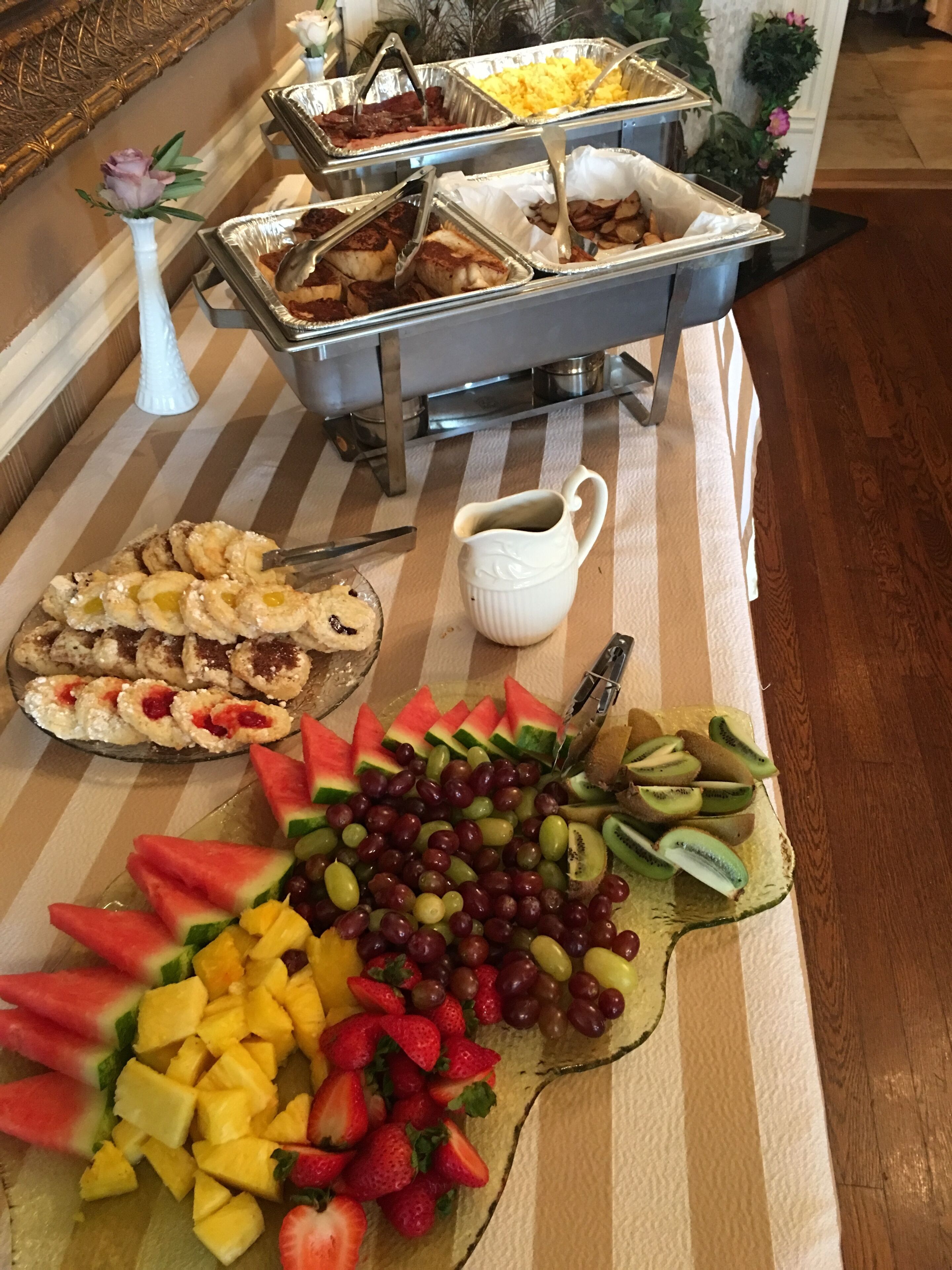 En buffetbod med forskellige retter, herunder frugt, grøntsager og desserter.