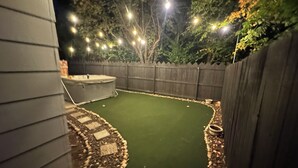 A backyard with a green artificial turf, a wooden fence, and a hot tub. - LUXURY GOLF GETAWAY DOWNTOWN BOISE (Boise)