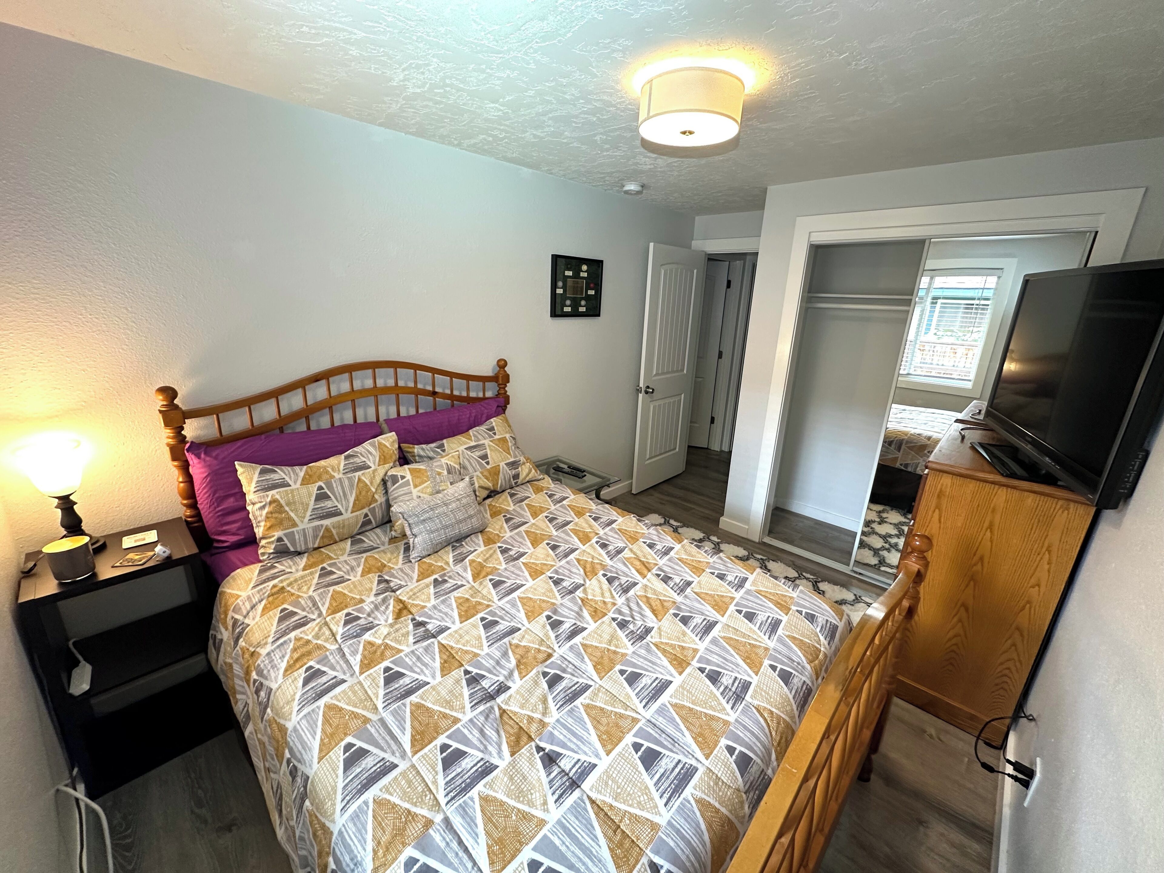 A bedroom with a bed, bedside table, lamp, and a television on a wooden cabinet.