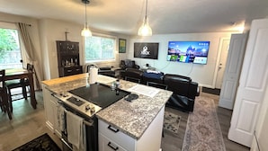 A modern kitchen with an island, a dining area, a living room with a TV, and a large window with curtains. - LUXURY GOLF GETAWAY DOWNTOWN BOISE (Boise)