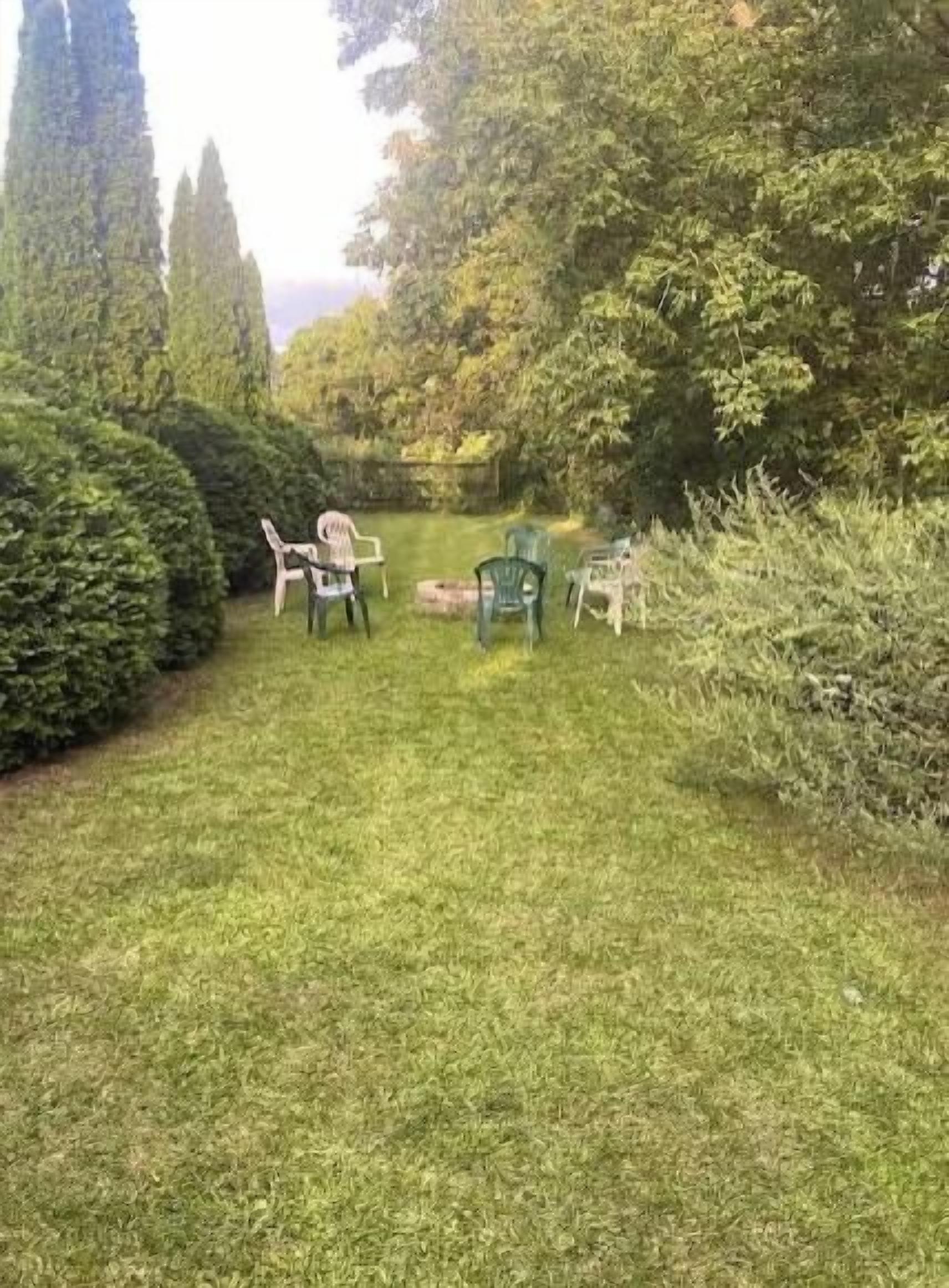 A grassy outdoor area with a table and chairs, surrounded by trees and shrubs.