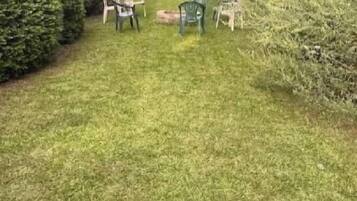 A grassy outdoor area with a table and chairs, surrounded by trees and shrubs.