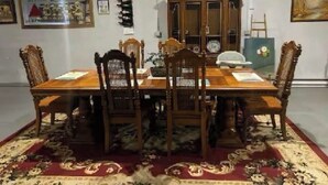 A dining room with a wooden table and chairs, a patterned rug, and a cabinet in the background.