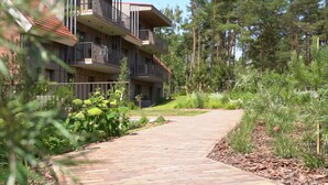 A multi-story building with balconies, surrounded by a wooded area and a paved walkway. - New 2025 Pervalka Neringa Flat White Dunes: AC, Heating, Private Balcony (Pervalka)