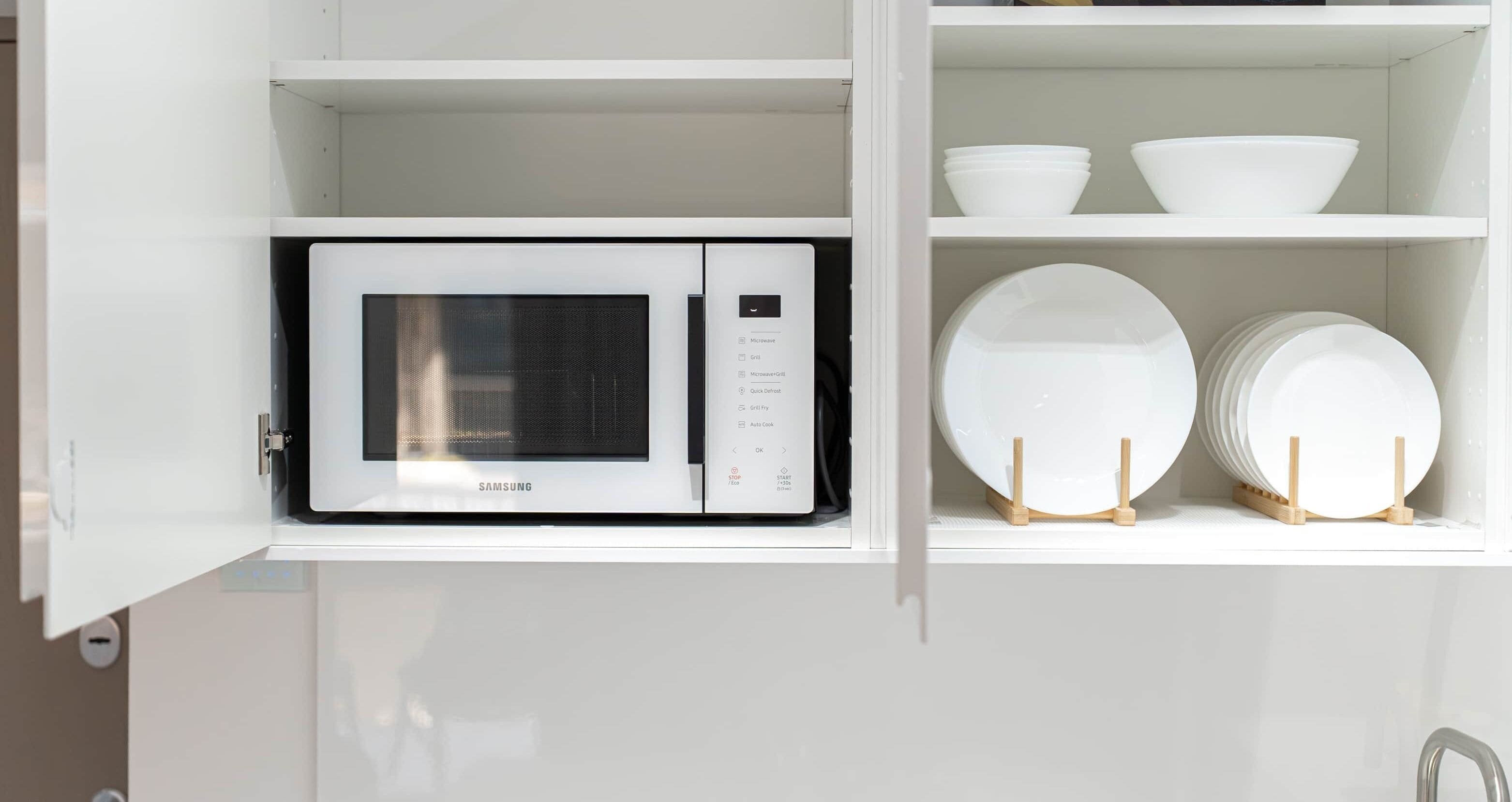 Una cocina blanca con un microondas y repisas que contienen boles y platos blancos.