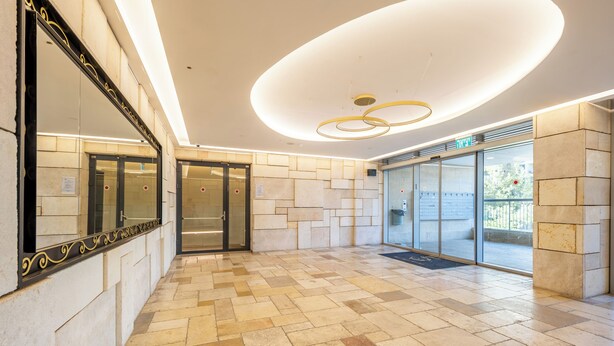 Un hall d’entrée moderne avec un sol carrelé, un grand miroir et un luminaire circulaire.