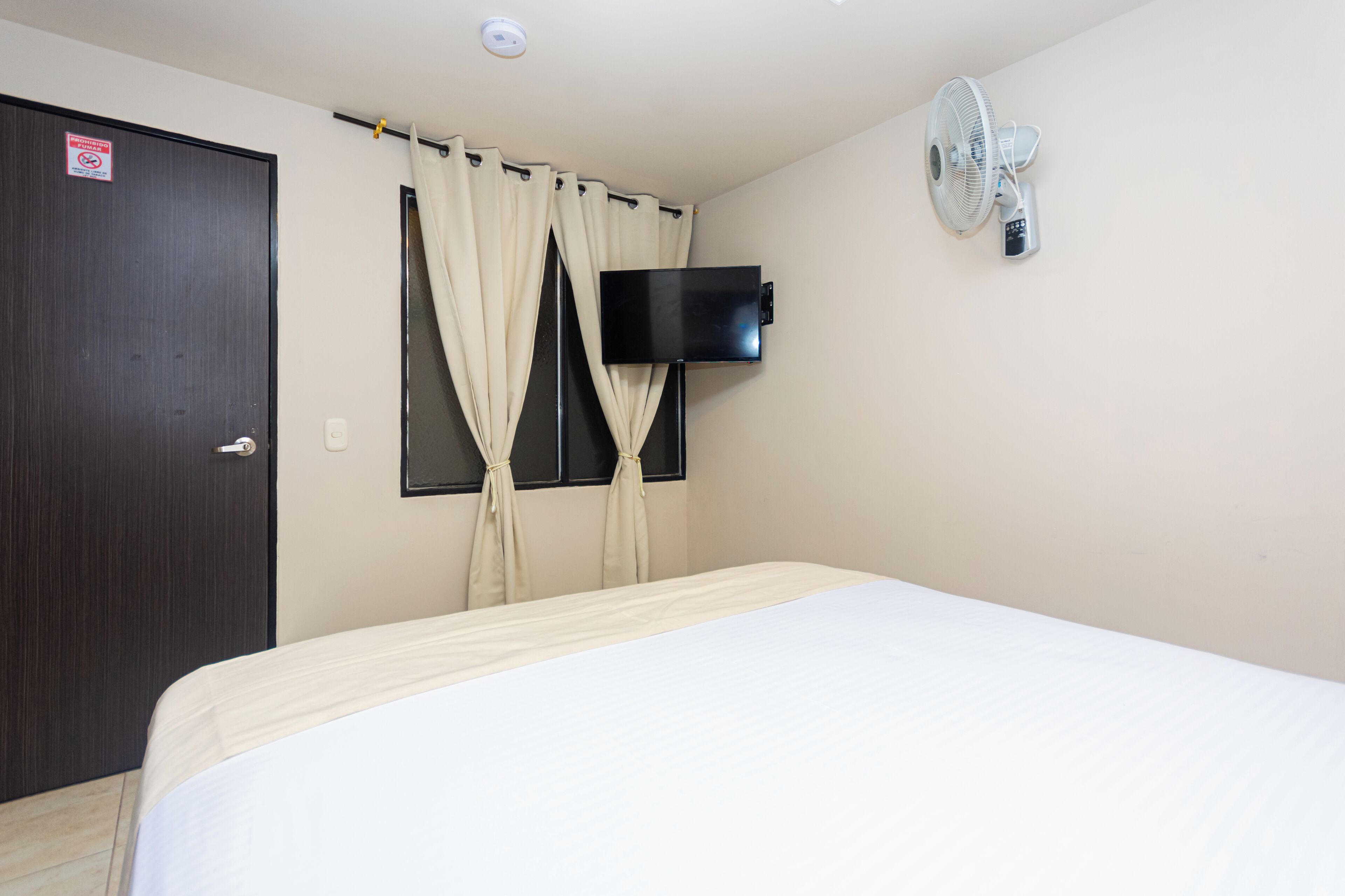 Habitación de hotel con cama, televisor montado en la pared, puerta y cortinas.