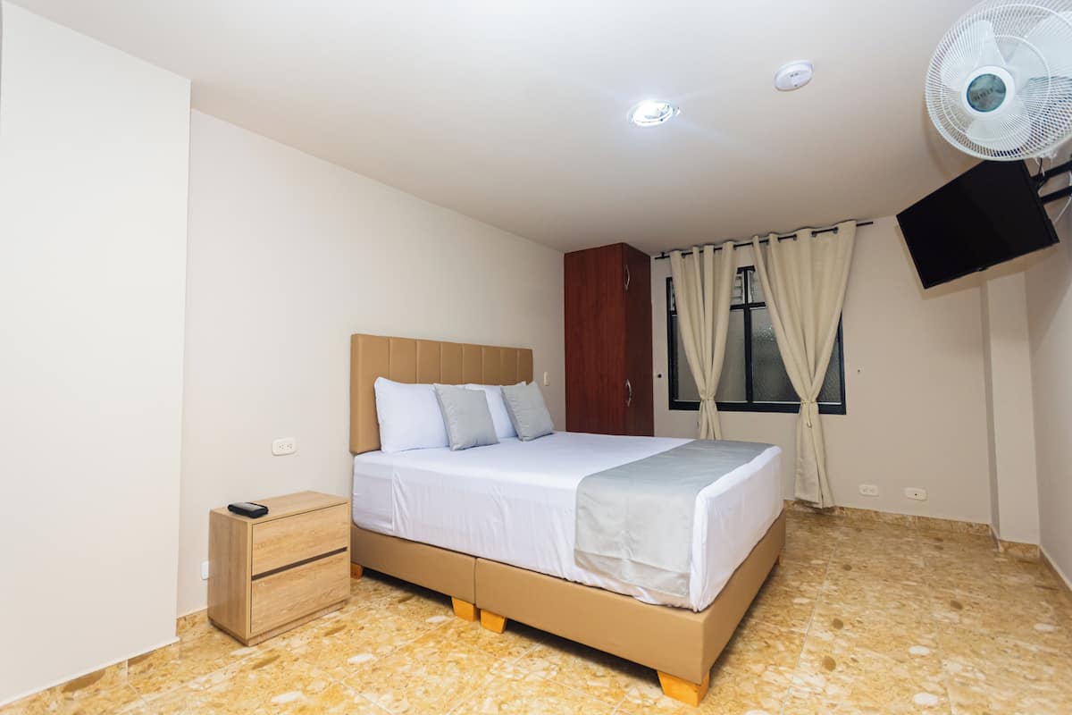 A bedroom with a bed, a nightstand, a TV mounted on the wall, and a ceiling fan.