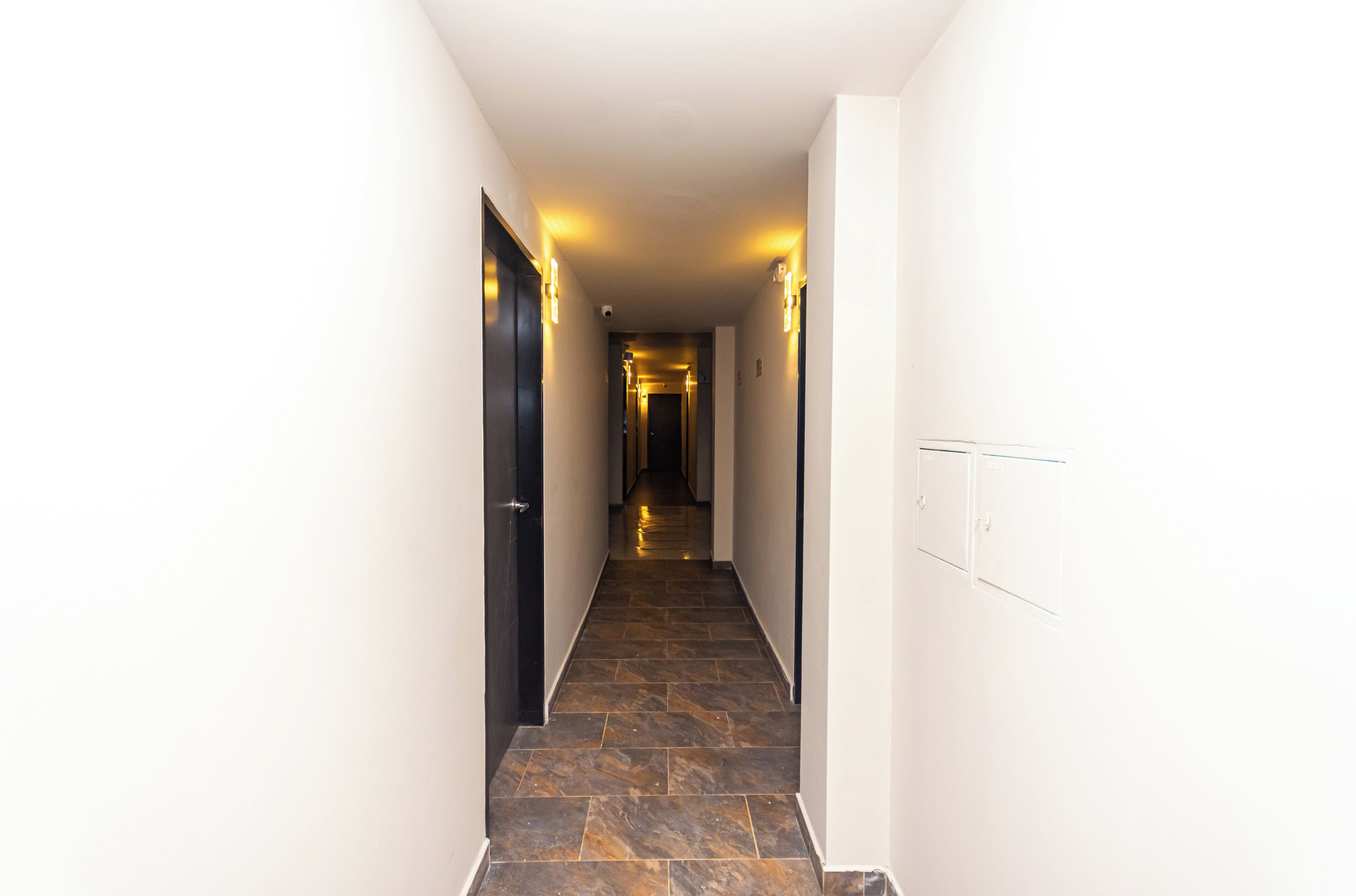 Un couloir doté d’un sol carrelé foncé, de murs blancs et de portes noires.