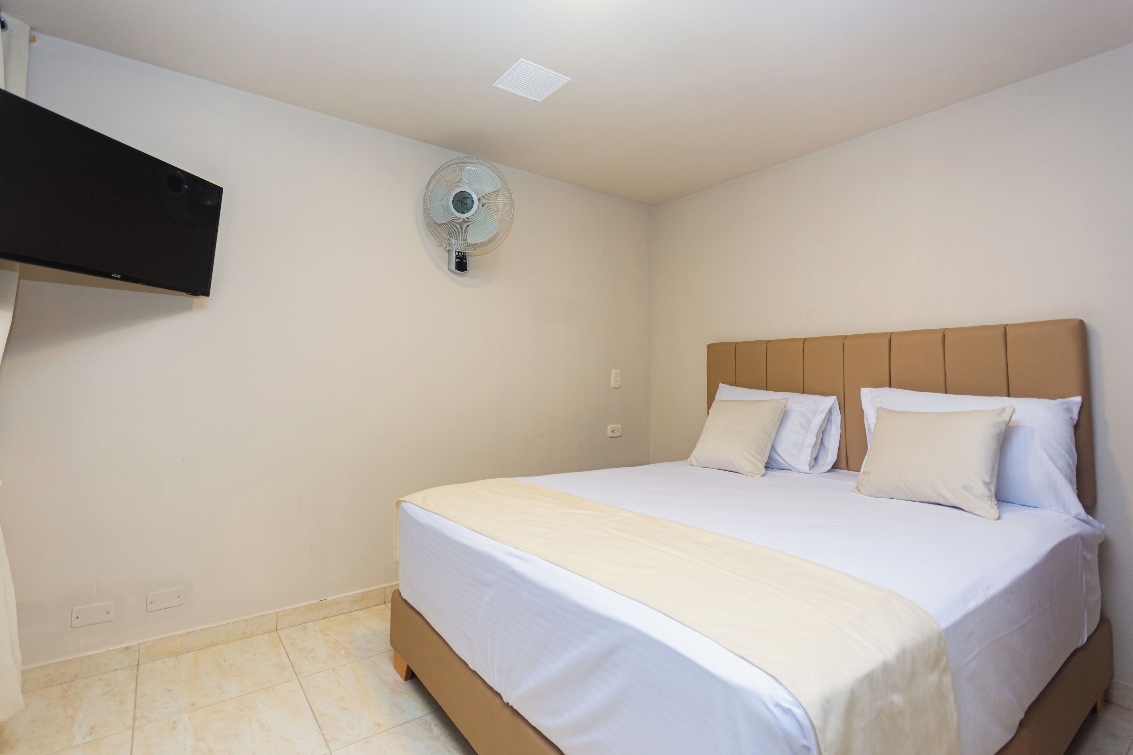 A bedroom with a bed, a wall-mounted fan, and a TV on the wall.