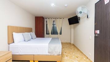 A bedroom with a bed, a wardrobe, a television mounted on the wall, and a ceiling fan.