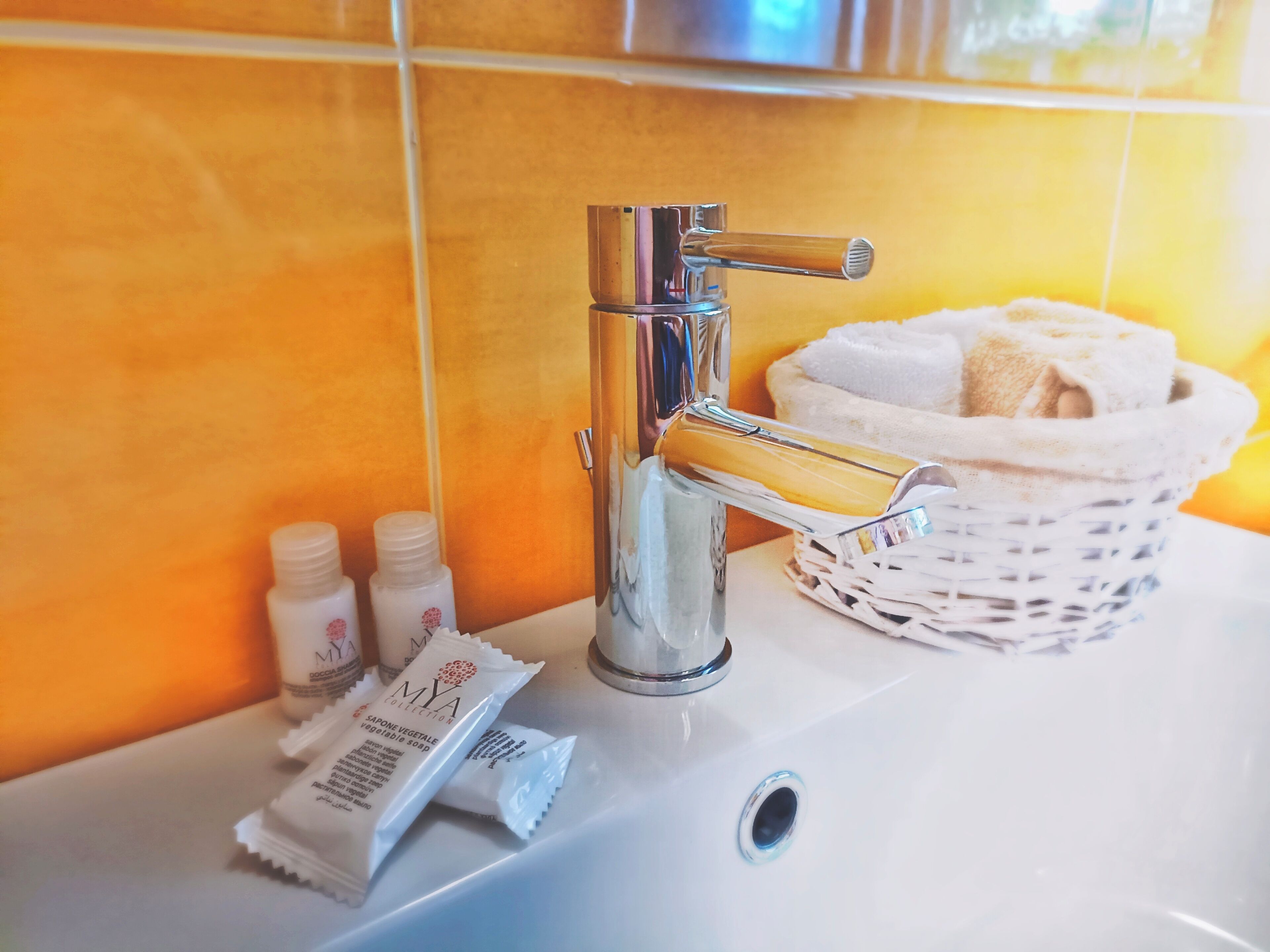 Ein Badezimmerwaschbecken mit einem Chromarmaturen, ein weißer Korbwicker mit Handtüchern und zwei kleine Seifenspender.