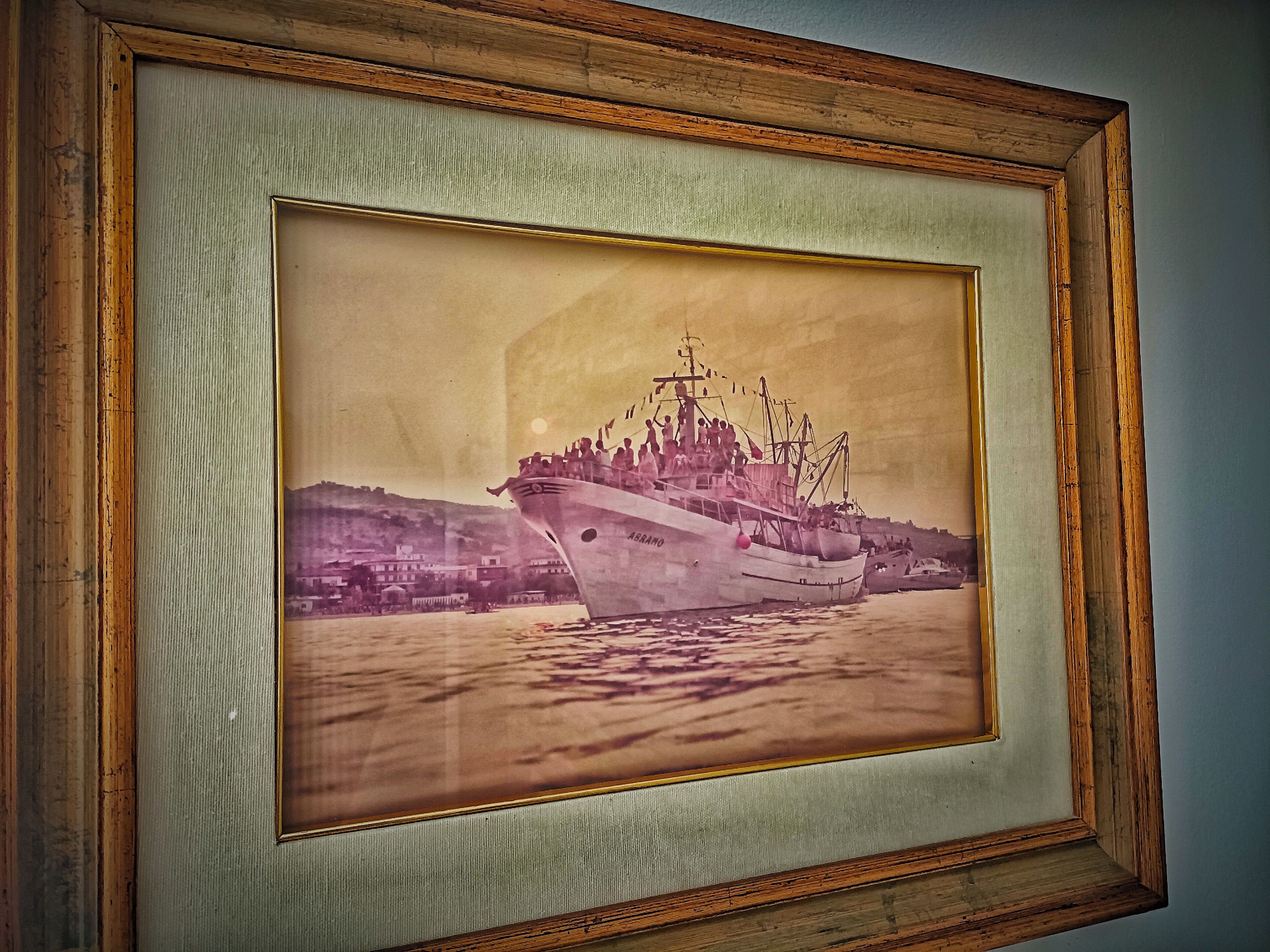 A framed photograph of a ship with the name "S.R.ANO" on its side, docked at a harbor with buildings in the background.