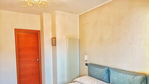 A hotel room with a wooden door, a radiator, a bed with white bedding, and a light blue headboard.
