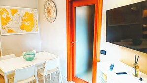 A room with a white table, chairs, a map on the wall, a clock, a door, and a TV.