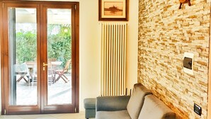 A modern living room with a stone wall, a wooden door leading to an outdoor area, a grey sofa, and a pendant light.