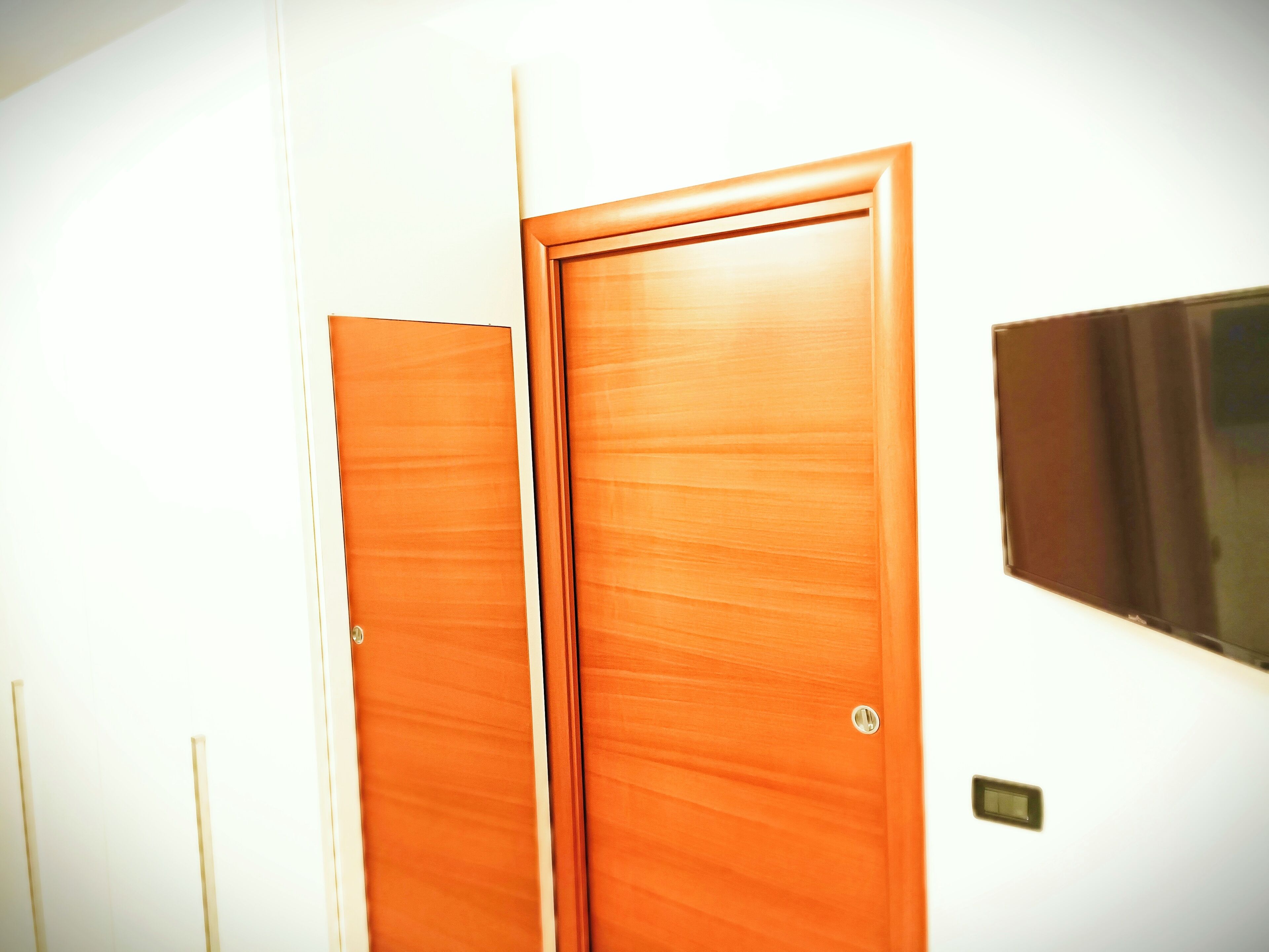 Une chambre d’hôtel avec deux portes en bois, un interrupteur fixé au mur et un petit objet rectangulaire accroché au mur.