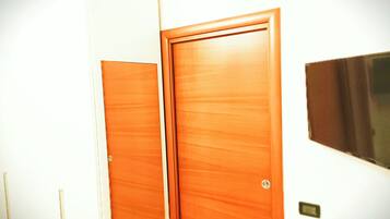 Une chambre d’hôtel avec deux portes en bois, un interrupteur fixé au mur et un petit objet rectangulaire accroché au mur.