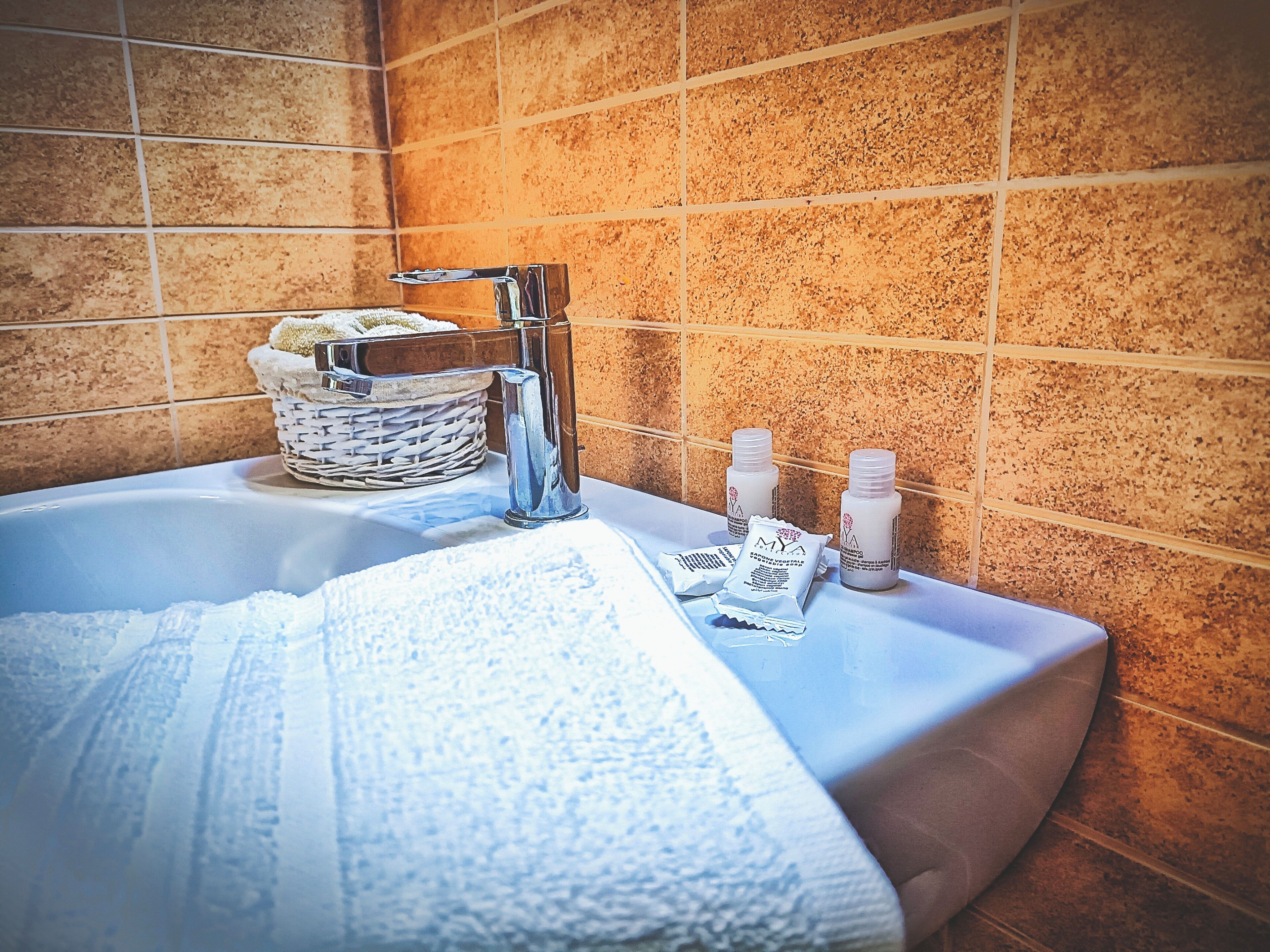 A bathroom with a bathtub, a white towel, a wicker basket, and two bottles of shampoo.