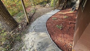 A stone pathway leading to a wooden staircase under a covered area with a view of a wooded landscape.