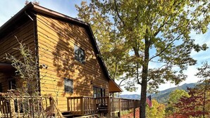 A wooden cabin with a porch, surrounded by autumn foliage and a view of mountains.