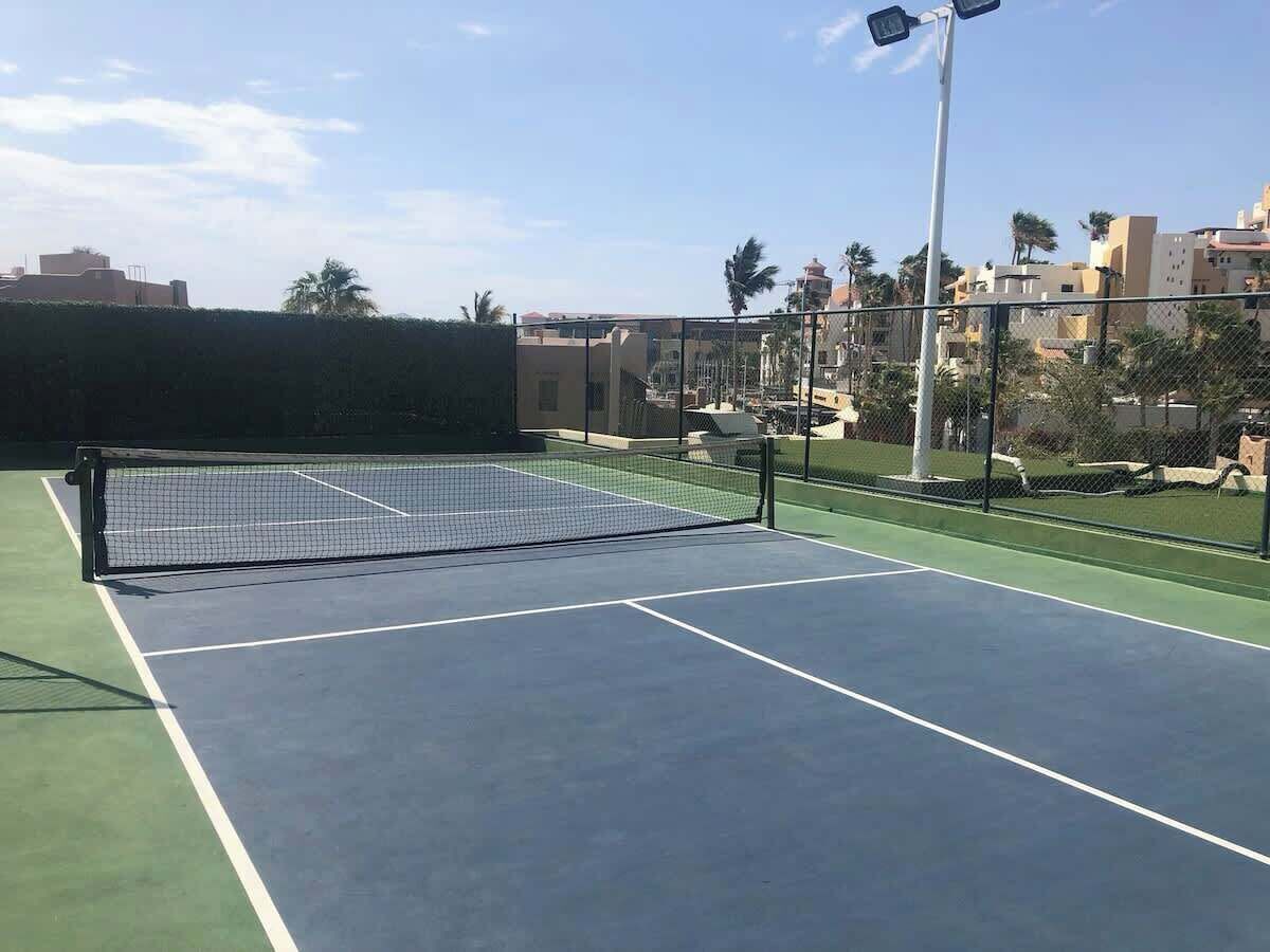 A tennis court with a net, surrounded by a fence and palm trees.