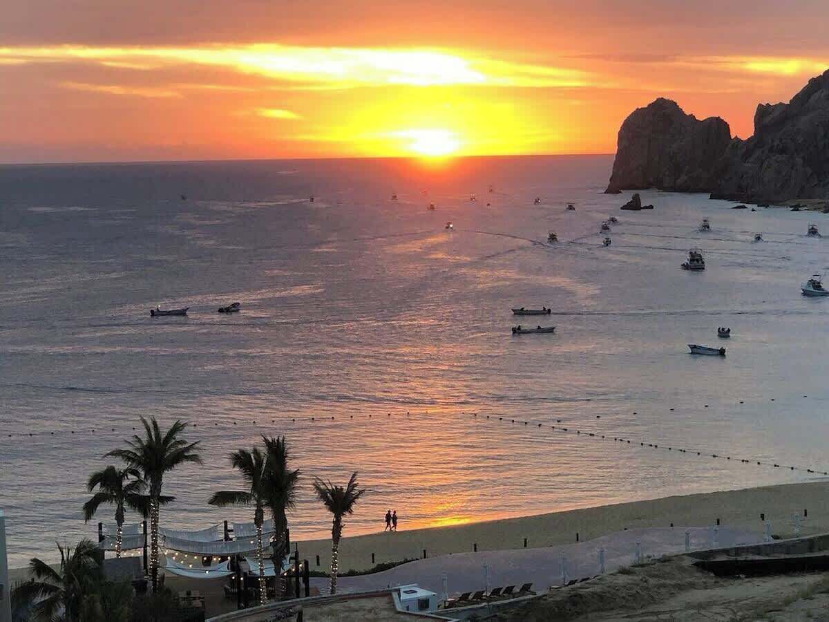 A beach with boats and palm trees during sunset.
