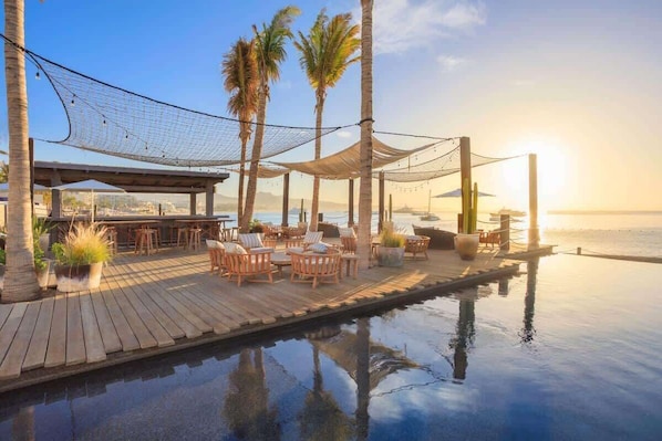 A wooden deck with outdoor seating, a pool, and palm trees.