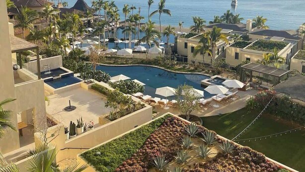 A resort with a pool, palm trees, and a view of the ocean. - Medano Beach Cabo Resort 3 Bedroom  (Cabo San Lucas)