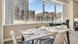 A modern dining area with a large window, a dining table set with plates and bowls, and a view of city buildings. - LAKE VIEW SkyTower Suite: Downtown ~ King Bed (Cleveland)