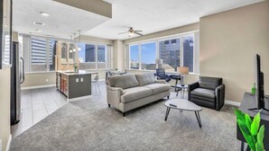 A spacious living area with a sofa, coffee table, and a TV. There is a kitchen area with a dining table and chairs. The room has large windows providing a view of the city. - LAKE VIEW SkyTower Suite: Downtown ~ King Bed (Cleveland)