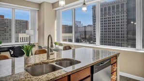Una cocina moderna con encimeras de granito, un lavamanos doble y lavavajillas. Cuenta con amplias ventanas y vistas a la ciudad.